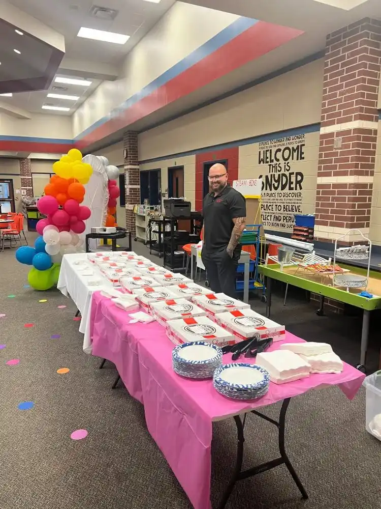 Table set with food and balloons at a community event in an elementary school.